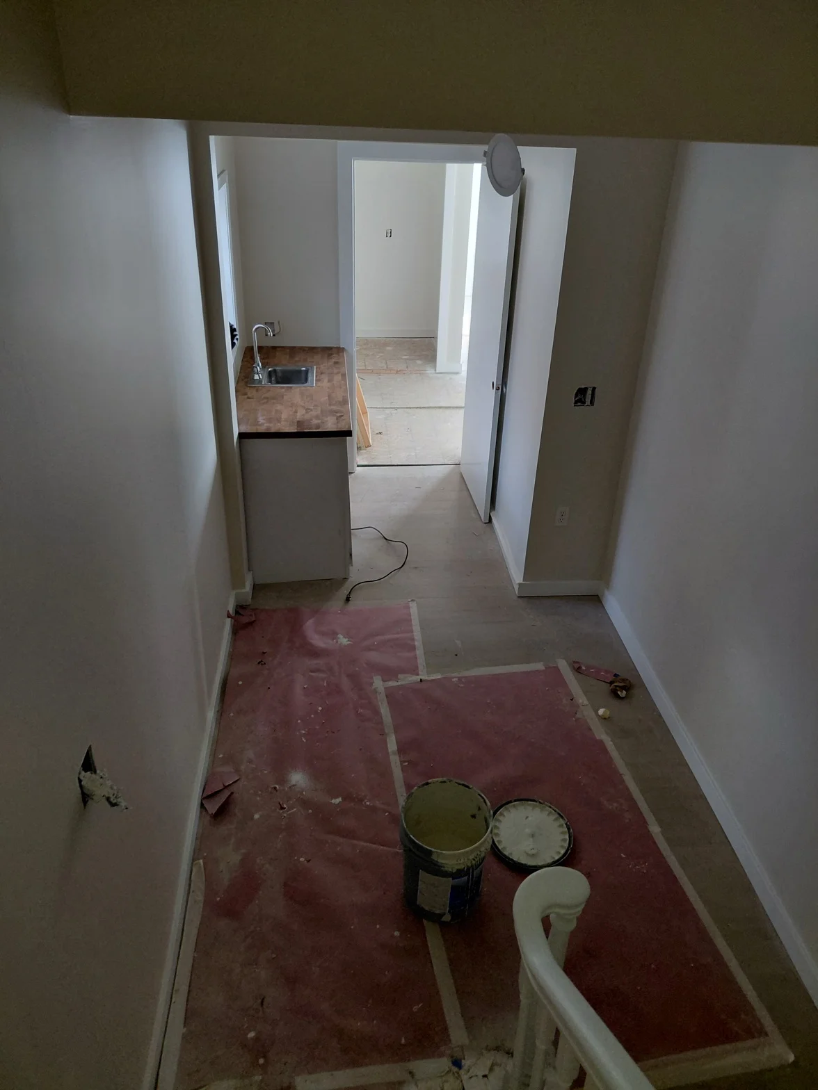 Residential interior mid-project with fresh drywall, paint supplies, and an open kitchen and living space