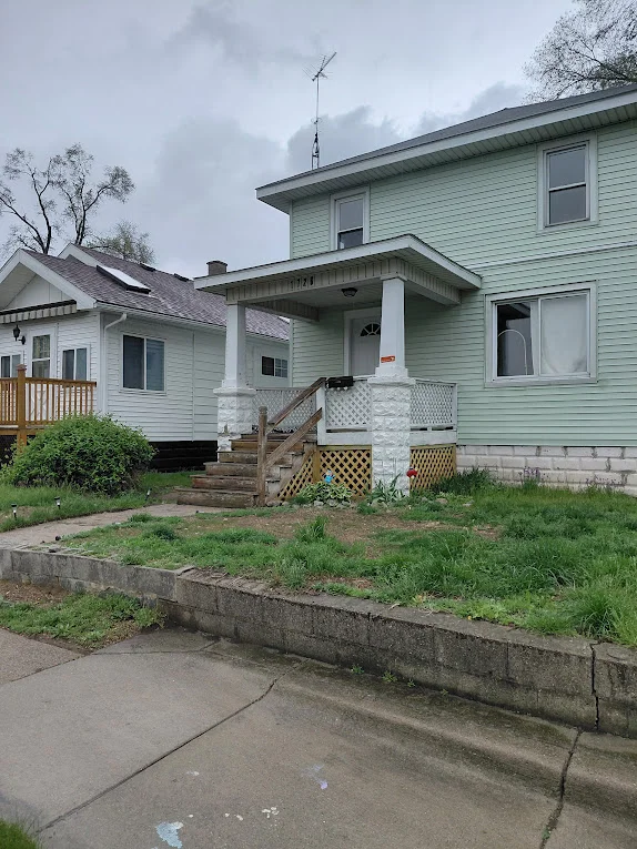 Light green two-story home with freshly painted white trim, a covered porch, and front steps