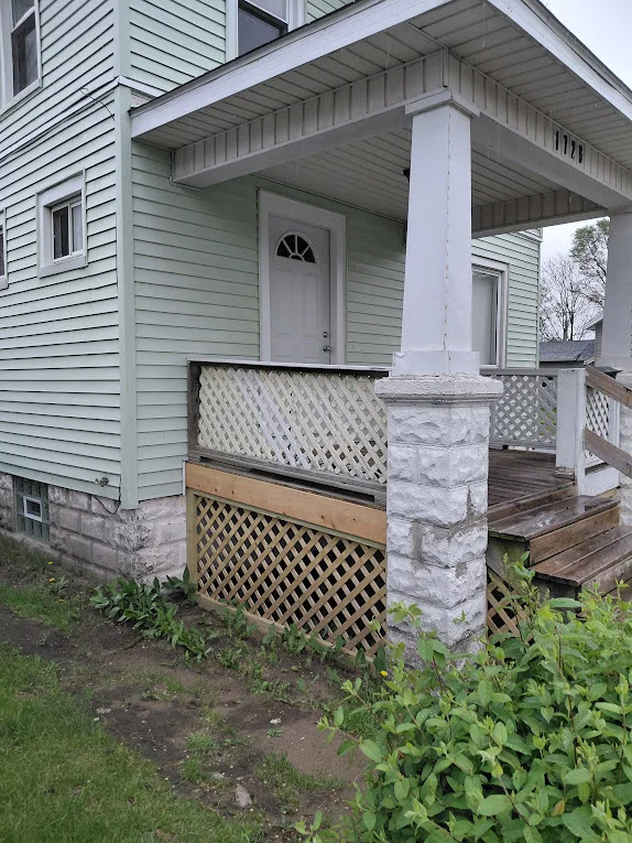Residential covered front porch with white columns, light green siding, and a white door