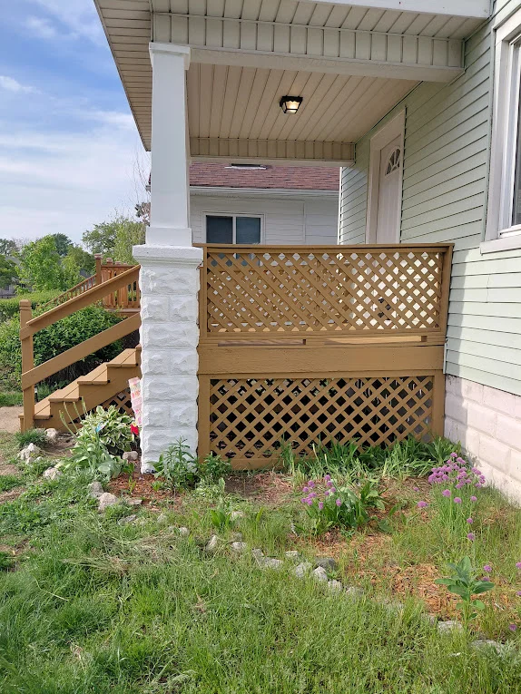 Residential deck with wooden lattice panels, white support columns, and landscaped garden beds